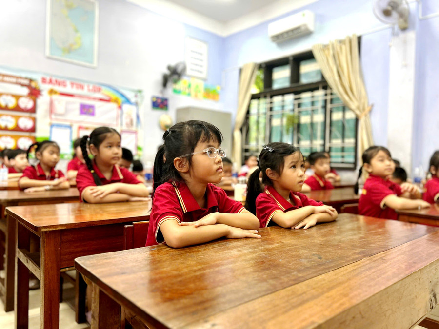 Học sinh ngồi ngay ngắn trong lớp học, đôi mắt mở to, tò mò trước bảng đen và phấn trắng. 9.jpg